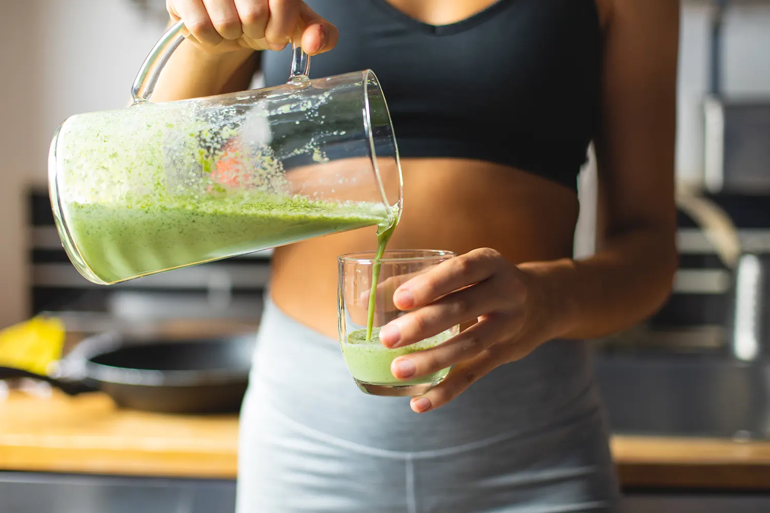 A woman pouring a green smoothie into a glass